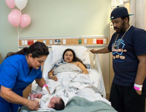 A Beverly Hospital nurse looks over a newborn baby while the mother and father watches