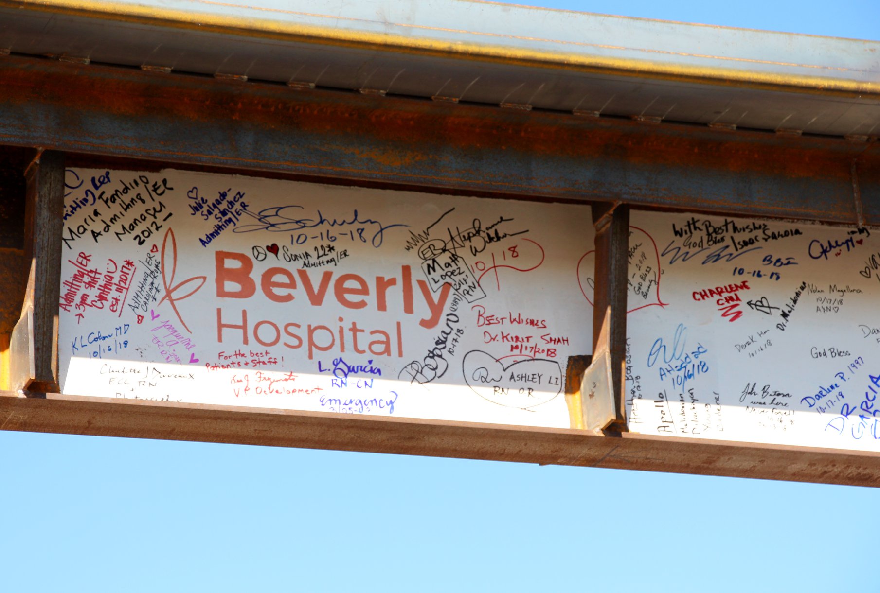A close up shot of the Beverly Hospital logo surrounded by several hospital staff signatures on the final metal beam