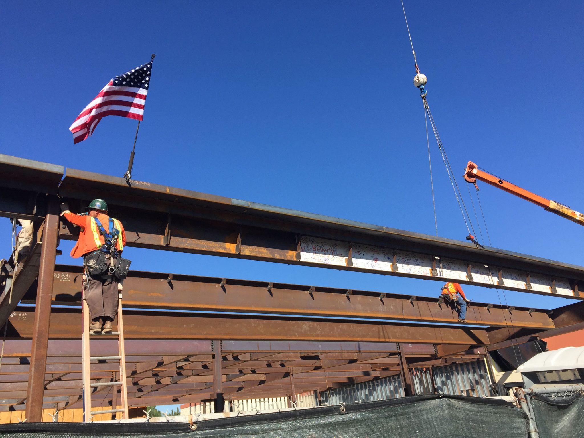 A construction worker on a ladder is securing the final metal beam at the Emergency Care Center expansion construction site
