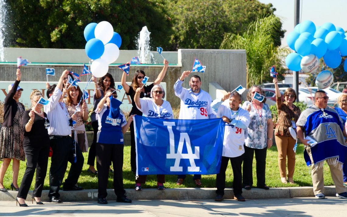 A close up front view of Beverly Hospital employees with Dodgers jerseys or flags waving to the passing cars.