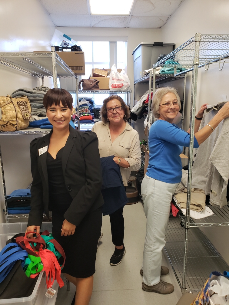 3 women from Rotary club smile at the camera while organizing Beverly Hospital's Heart of Compassion closet