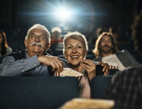 Close up of a senior couple eating popcorn and enjoying a movie in the cinema