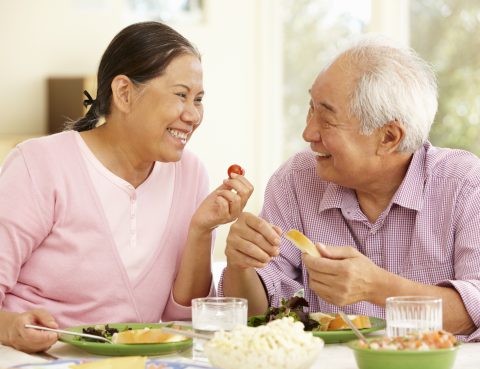 Senior asian couple sharing meal at home smiling at one another