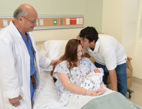 OBGYN Stephen Lee smiles as his patient holds her baby and receives a kiss on the forehead from her significant other