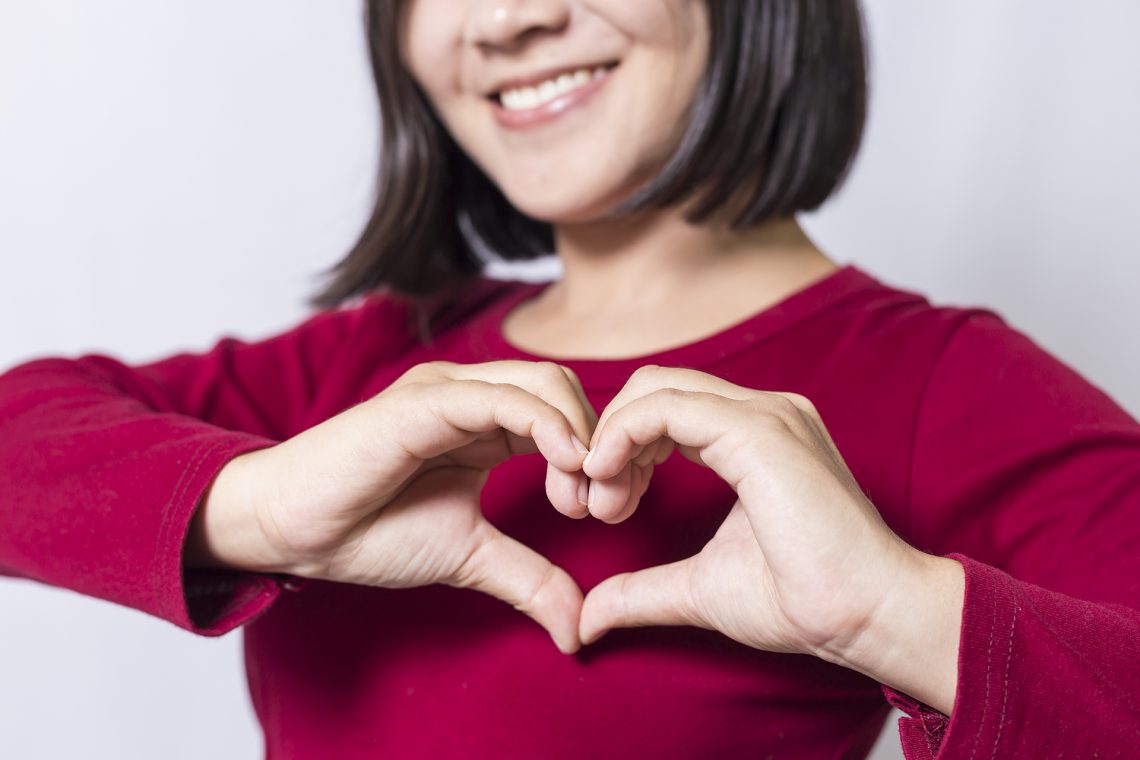 Woman in red shirt makes a heart with her hands over her chest