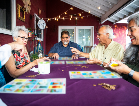Hispanic seniors smile as they play loteria in the backyard
