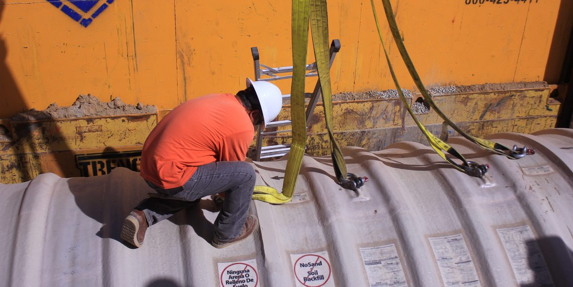 A construction worker works to unlatch the harness straps from the emergency generator fuel tank after it is lowered into the ground