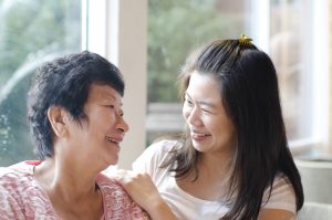 Elderly asian mother and adult asian daughter smile and look at each other indoors