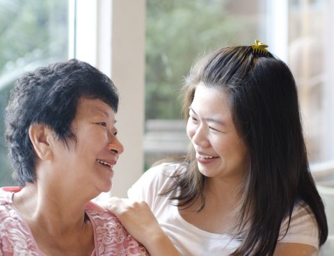 Elderly asian mother and adult asian daughter smile and look at each other indoors
