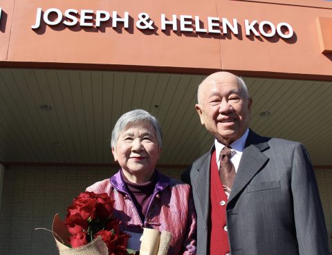 Mr. Joseph Loo and Dr. Helen Koo smile and pose under a sign with their names outside at the Emergency Room naming ceremony