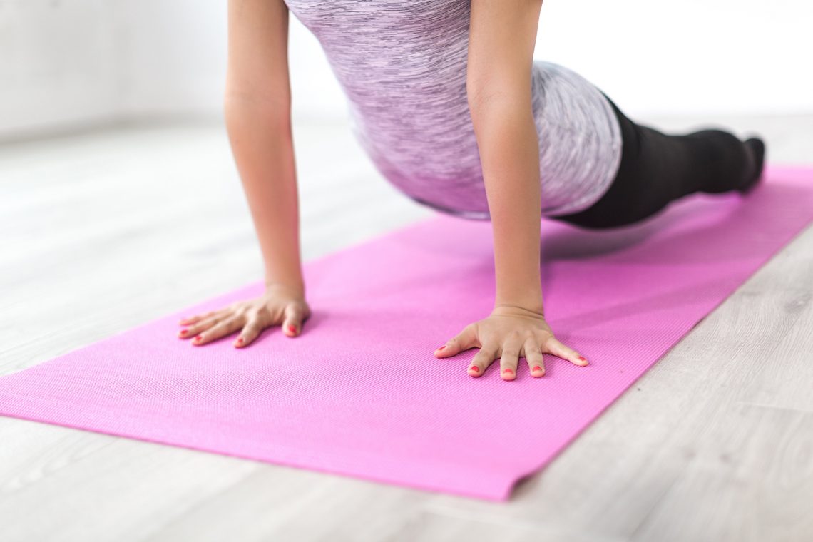 Lower half of woman stretching upwards in cobra pose on pink yoga mat