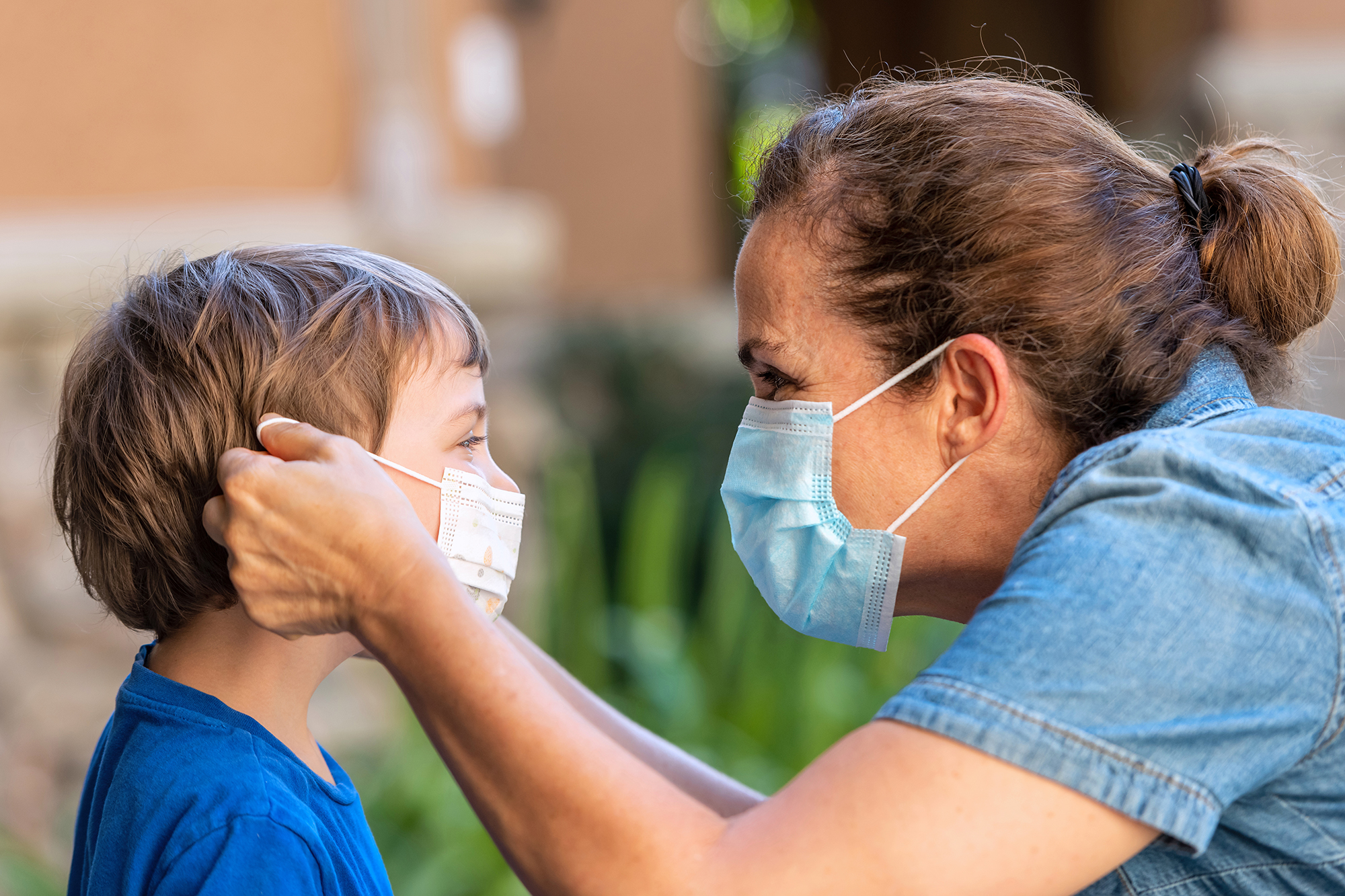 Mature woman and son face to face as she is putting on him a protective face mask