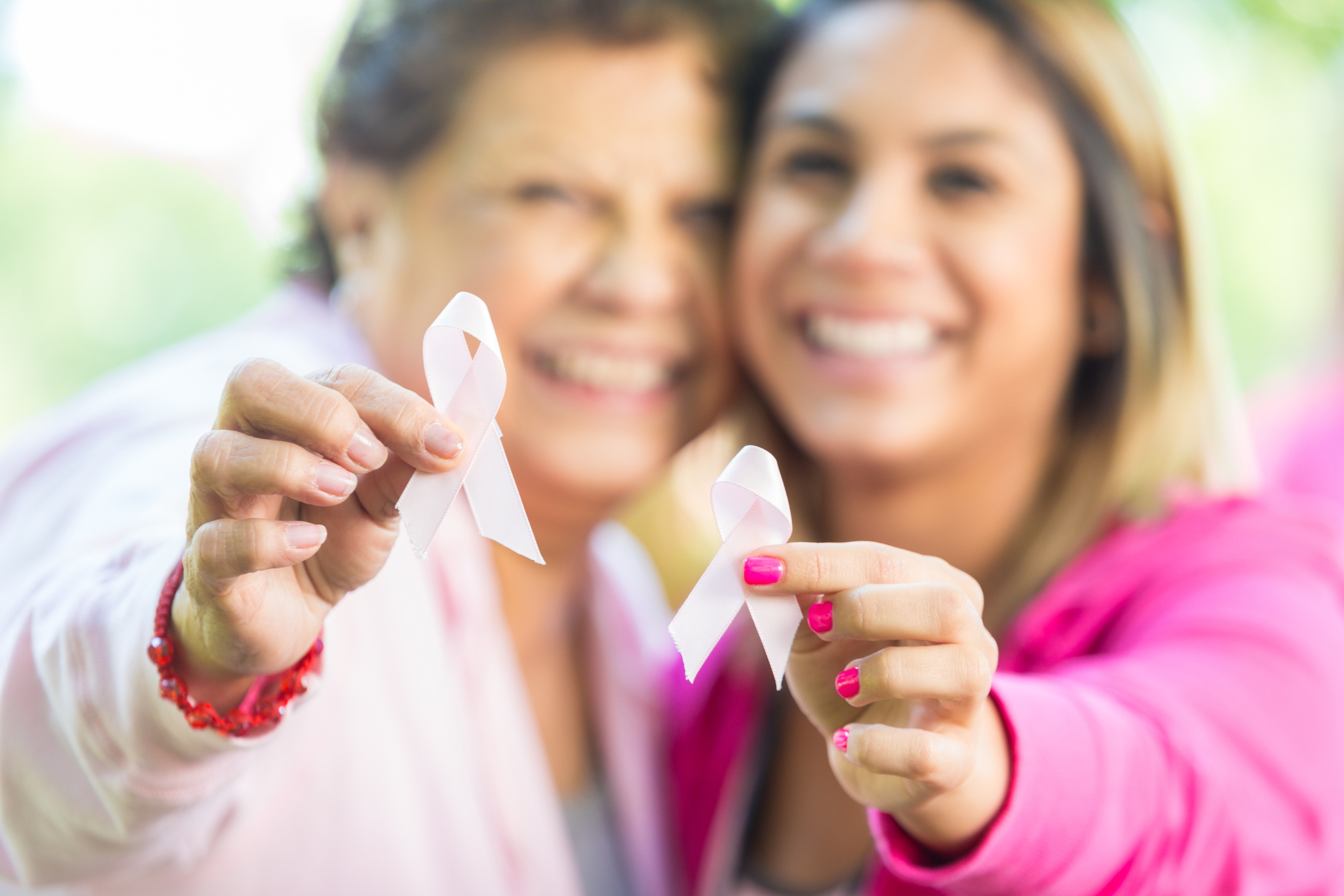 Senior Hispanic woman and adult daughter smile and hold up pink breast cancer awareness ribbons