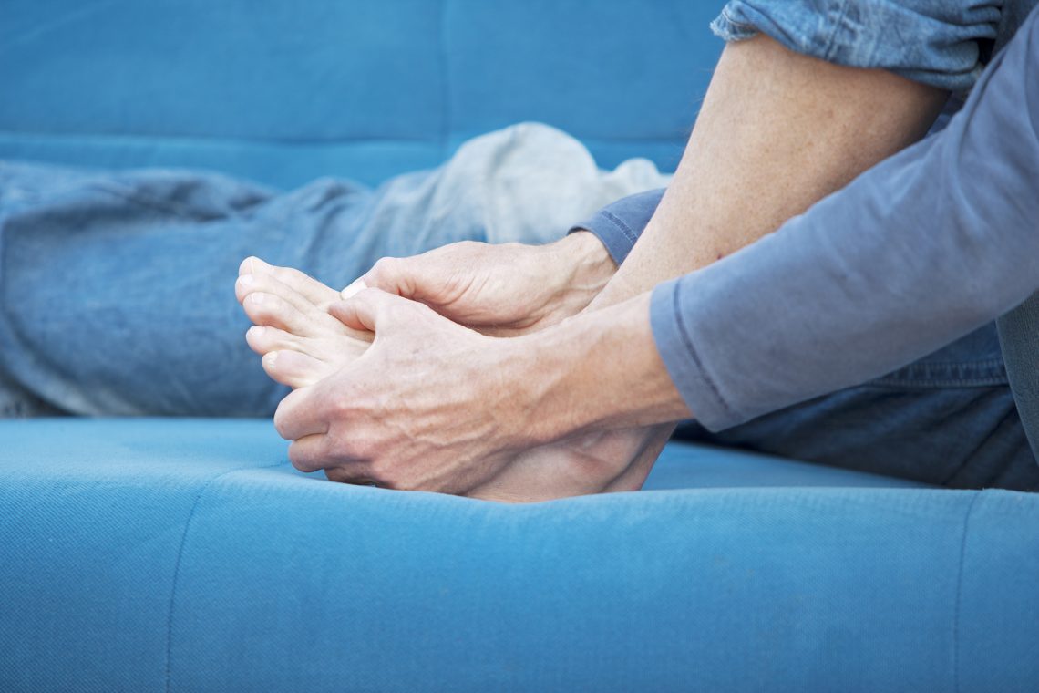 Close up of senior sitting on couch and examining foot for foot pain or any wounds