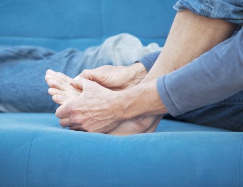 Close up of senior sitting on couch and examining foot for foot pain or any wounds