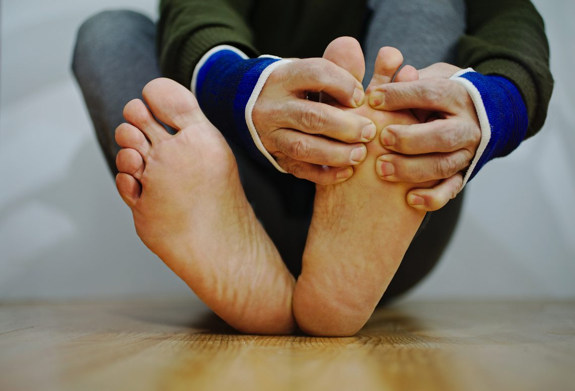 Close up of person sitting on floor checking their feet for wounds