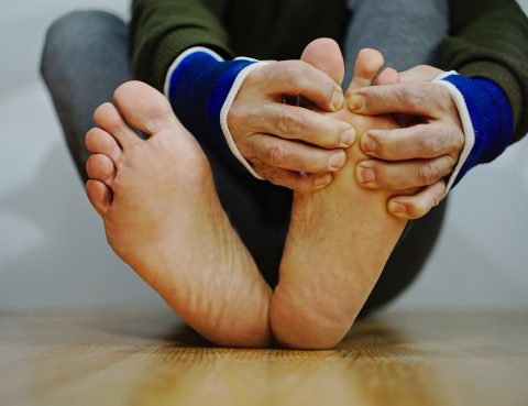 Close up of person sitting on floor checking their feet for wounds
