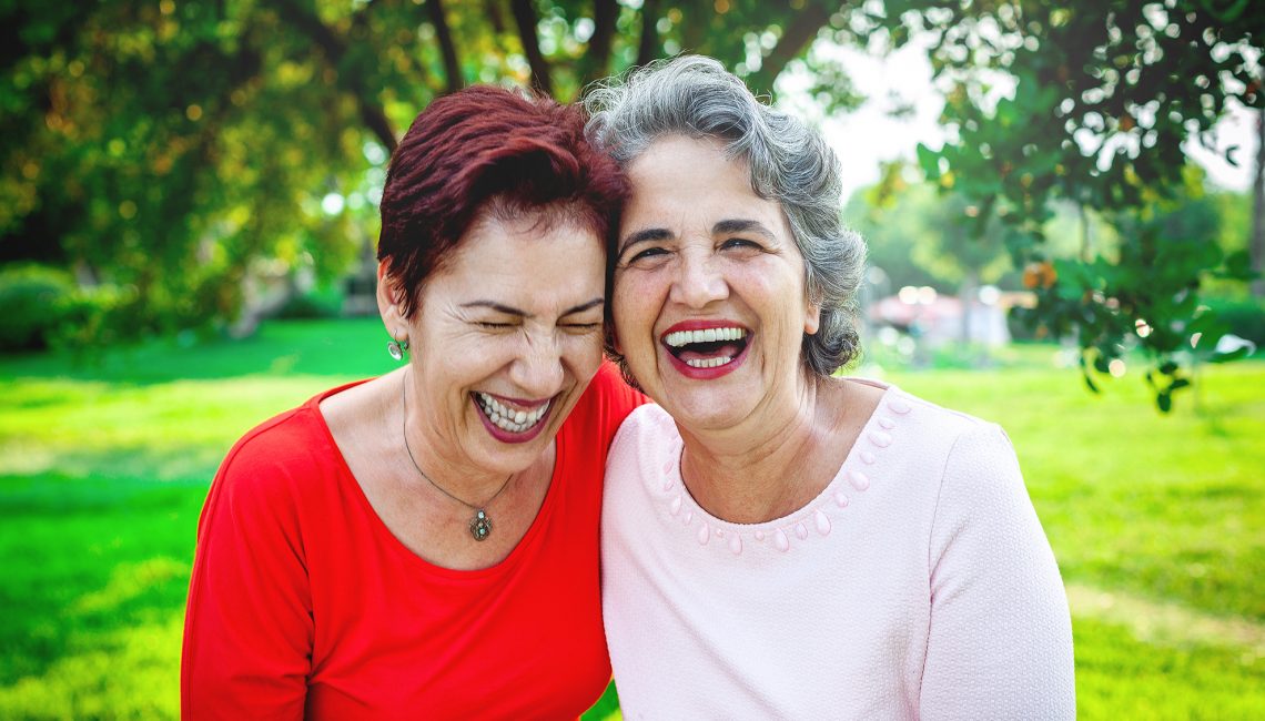 Two senior women holding each other and laughing outside