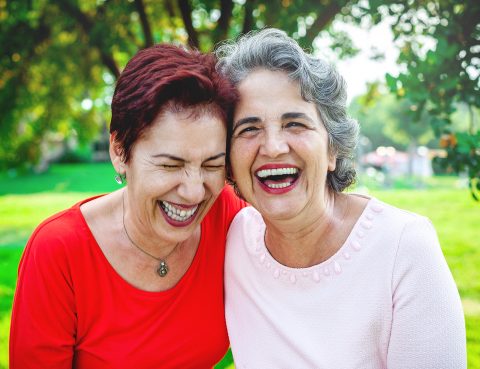 Two senior women holding each other and laughing outside