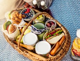 Variety of sandwiches and fruits in a wicker basket on a picnic blanket