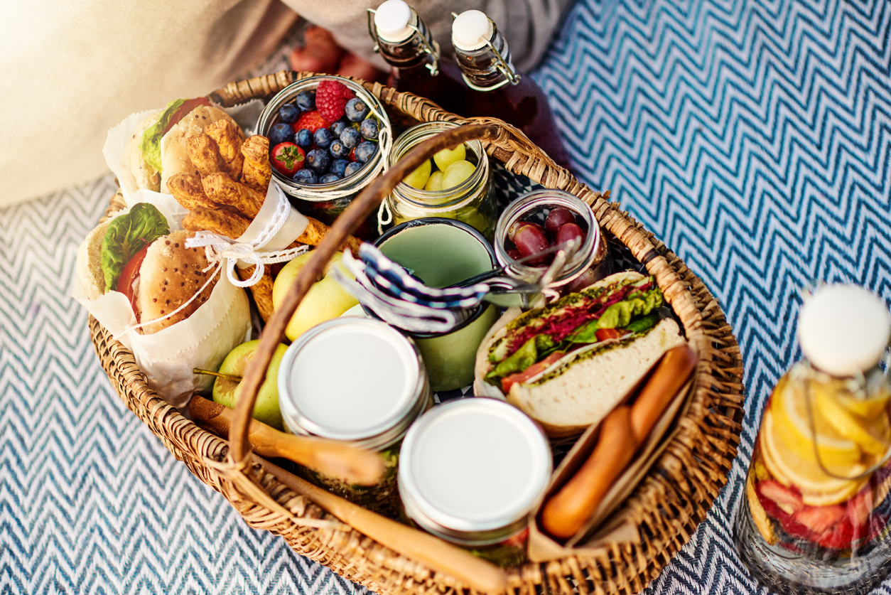 Variety of sandwiches and fruits in a wicker basket on a picnic blanket