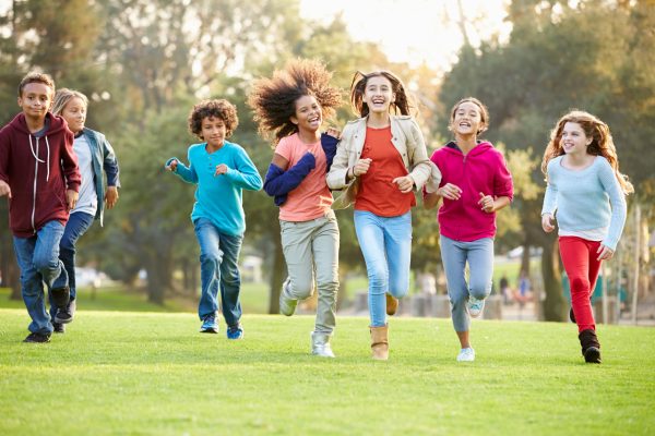 Group Of Smiling Young Children In The Park Running Towards The Viewer
