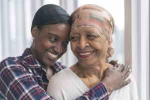 Smiling black senior woman who has cancer being hugged by her supportive adult daughter