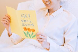 Close up of female patient in hospital bed reading yellow get well soon card.