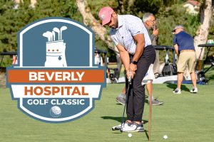 Man practicing his golf putt with the Beverly Hospital Golf Classic logo on his left.